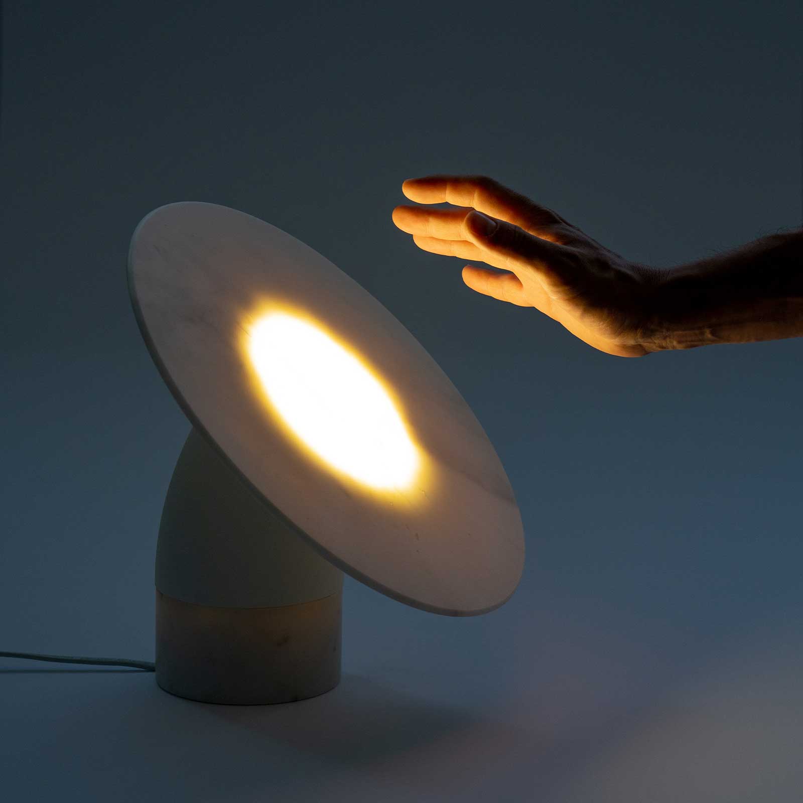 Translucent marble table lamp Aura, lit; hand hovering above the disc